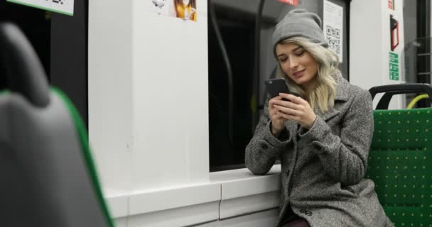 Vacker blond flicka på telefonen ringer upp meddelandet i publick transport. Kvinnan ler och skriva med två fingrar. — Stockvideo