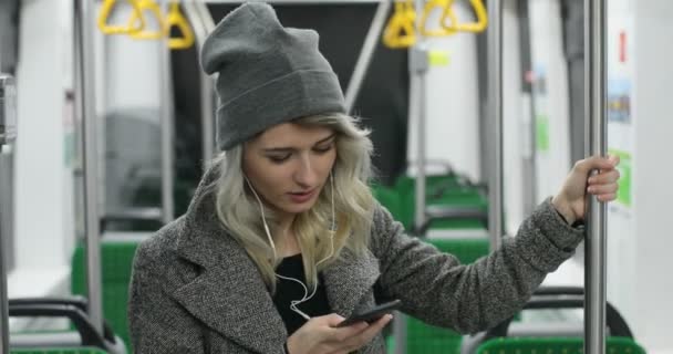 Portrait de fille mignonne dans les écouteurs écoutant de la musique et naviguant sur le téléphone mobile dans les transports publics. Elle tient la main courante 