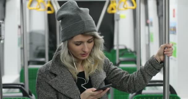 Aranyos lány fejhallgató hallgató-hoz zene és szemöldök-ra mozgatható telefon-ban nyilvános szállítás portréja. Ő tartja a kapaszkodó — Stock videók