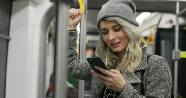 Mujer joven sonriente con auriculares que responden a una llamada entrante en el transporte público — Vídeo de stock