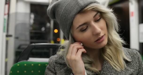 Retrato de una linda chica usando auriculares y escuchando música en el teléfono móvil en el transporte público. Ciudad luces fondo — Vídeo de stock