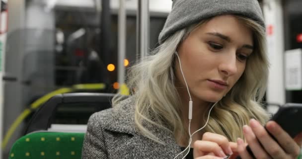 Retrato de menina bonito em fones de ouvido ouvir música e navegação no telefone móvel no transporte público. Cidade luzes fundo — Vídeo de Stock