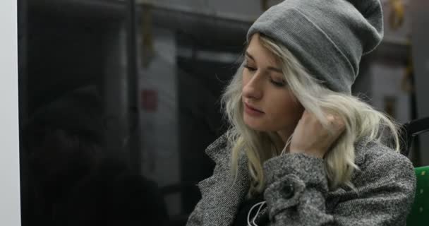 Linda chica usando auriculares y escuchando música en el teléfono móvil en el transporte público. Ciudad luces fondo — Vídeos de Stock