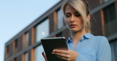 Yakın çekim portre tutarak ve dışında kameraya bakarak gülen tablet kullanarak güzel bir iş kadını. Modern mimari bina arka plan