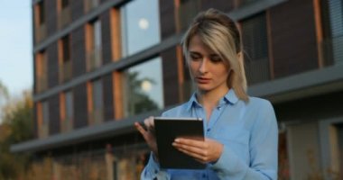 Yakın çekim portre tutarak ve dışında kameraya bakarak gülen tablet kullanarak güzel bir iş kadını. Modern mimari bina arka plan