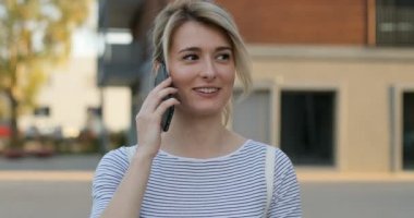 Konuşmayı cep telefonunda yürüyüş sırasında arka bina sokak, modern mimarisi üzerinde güzel genç kadın