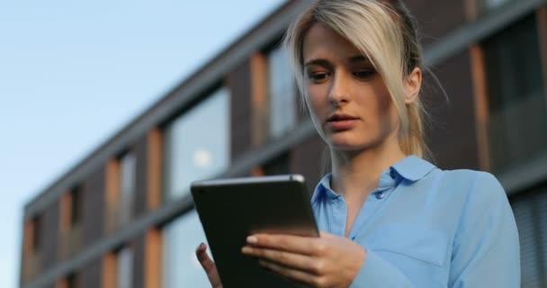 Retrato de cerca de una hermosa mujer de negocios sosteniendo y usando la tableta afuera, sonriendo mirando a la cámara. Edificio de arquitectura moderna fondo — Vídeo de stock