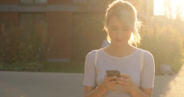 Gelukkig mooi meisje met behulp van slimme telefoon in de stad, zomer meisje portret. Jonge vrouw met smartphone lopen in de stad — Stockvideo