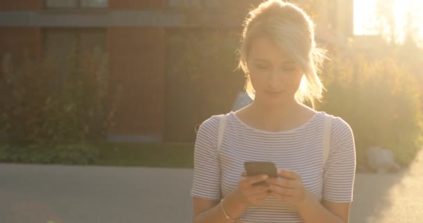 Feliz chica hermosa usando el teléfono inteligente en la ciudad, retrato de niña de verano. Mujer joven con smartphone caminando por la ciudad — Vídeos de Stock