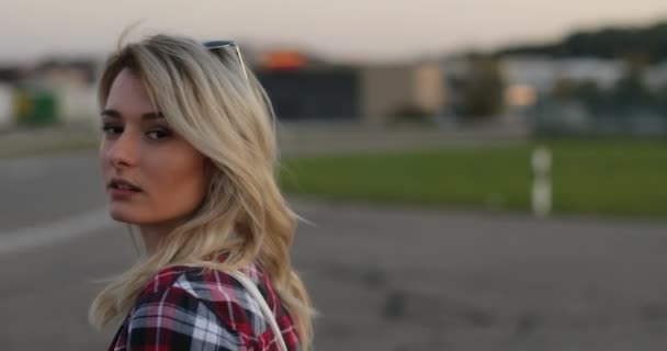 Attraktive junge blonde Mädchen mit einer San-Brille auf dem Kopf läuft die Straße hinunter, dreht sich in die Kamera und lächelt. — Stockvideo