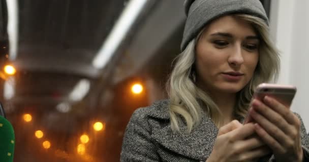 在公共交通工具上旅行时, 金发女郎在她的手机上浏览。夜城灯 — 图库视频影像