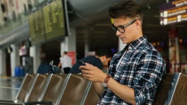 Havaalanı dinlenme odasında otururken akıllı telefon kullanarak bardaklarda çekici bir adam. Yan görünüm.