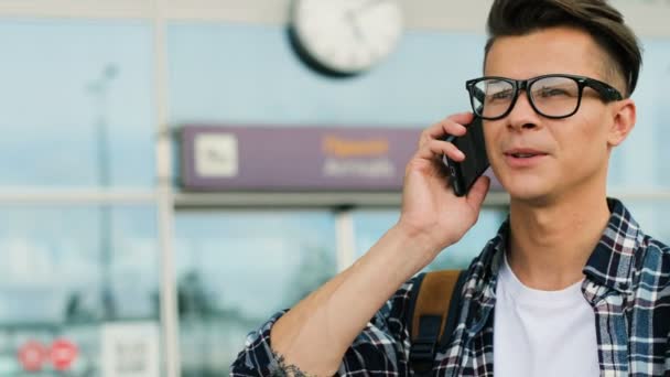 Portret van de jonge stijlvolle man praten met vrienden op de slimme telefoon op de achtergrond van de moderne luchthaven. Close-up. — Stockvideo