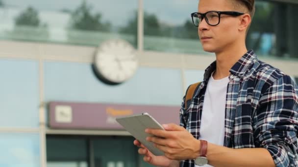 Joven hombre con estilo en gafas utilizando tableta en el fondo del aeropuerto moderno. De cerca. . — Vídeo de stock