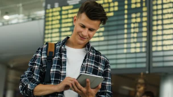 Attraktive lächelnde Mann in lässigem Hemd mit Tablet für die Überprüfung der Fahrkarte auf dem Ankunftstisch Hintergrund. Nahaufnahme. — Stockvideo