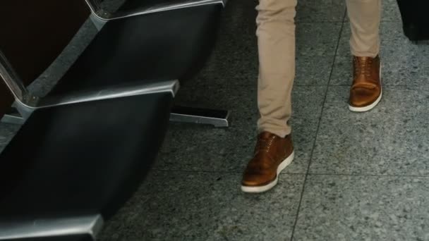 Joven hombre caucásico caminando al salón y sentado en el banco y esperando su vuelo. Vista desde atrás . — Vídeos de Stock