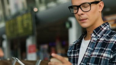 Biriyle sohbet ve havaalanı dinlenme odasında otururken kahve içmek için tablet kullanarak rahat tişörtlü genç adam.