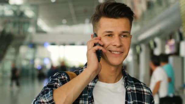 Close up portrait of young man in the walking in the modern airport terminal and talking on smart phone with friends. — Stock Video