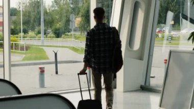 Yakışıklı delikanlı ile modern Havaalanı terminal penceresine yürüyen Bagaj. Dolly vurdu.