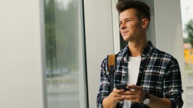 Pencere arka plan üzerinde sohbet için akıllı telefon kullanan genç çekici adam portresi.