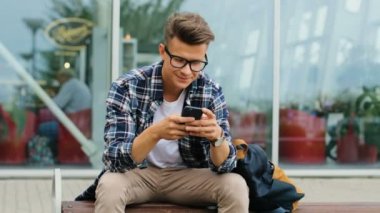 Çekici bir adam akıllı telefon sohbet yakınındaki bankta otururken kullanarak gözlük.