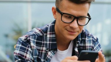 Akıllı telefon sohbet yakınındaki bankta otururken kullanarak bardaklarda çekici bir adam portresi.