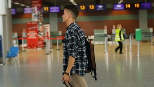 Joven hombre guapo con el equipaje caminando en la moderna terminal del aeropuerto. Dolly disparó. De cerca. Vista lateral . — Vídeo de stock