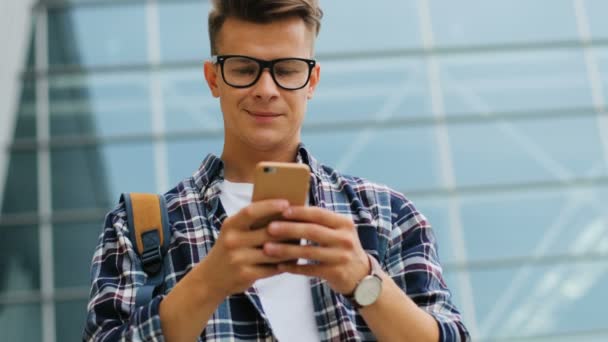 Retrato de jovem nos óculos na camisa elegante casual usando telefone inteligente no fundo do aeroporto . — Vídeo de Stock
