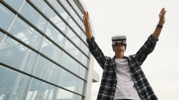 Joven hombre caucásico usando gafas de realidad virtual para jugar en el fondo del aeropuerto moderno. Vista desde la parte inferior . — Vídeos de Stock