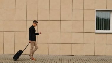 Şık genç adam akıllı telefon yazarken terminal Havaalanı'na yürüyüş bagaj ile.