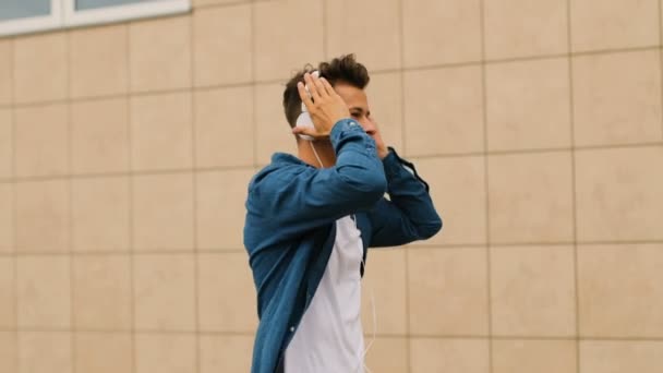 Primer plano de atractivo hombre feliz escuchando la música en los auriculares y bailando mientras camina cerca del aeropuerto . — Vídeos de Stock