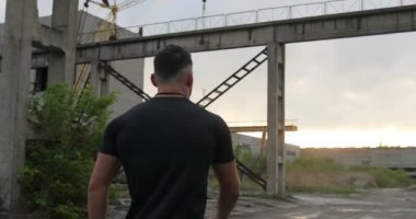 Endüstriyel kentsel park boyunca yürüyüş ve uzağa bakarak sağlıklı genç spor adamı portresi. Kendine güvenen genç adam hazır iş.