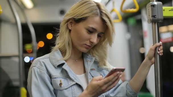 Portret Ładna dziewczyna w słuchawkach posiada poręczy, słuchania muzyki i przeglądania na telefon komórkowy w transporcie publicznym. Tle światła miasta — Wideo stockowe