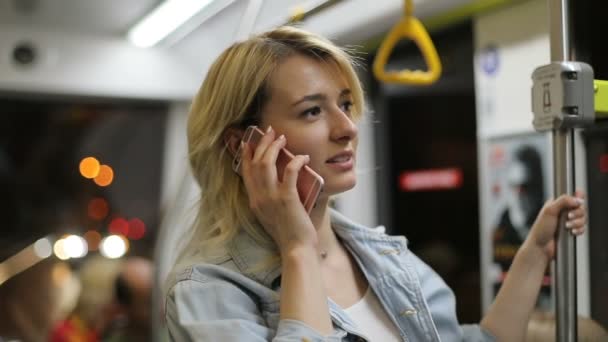Porträt einer hübschen jungen blonden Frau, die am Telefon telefoniert und Handläufe in öffentlichen Verkehrsmitteln hält. jemand, der anruft, Stadtbeleuchtung Hintergrund während der Fahrt in den öffentlichen Verkehrsmitteln — Stockvideo