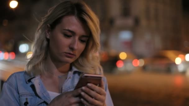 Ritratto di donna utilizzare il telefono cellulare di notte. Luci di città sfondo. Ragazza puntando il dito sullo smartphone schermo sullo sfondo illuminazione bokeh luce di colore nella notte, mani sms cellulare — Video Stock