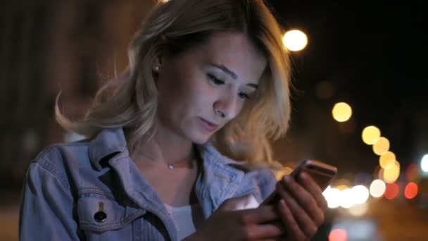 Ritratto di donna utilizzare il telefono cellulare di notte. Luci di città sfondo. Ragazza puntando il dito sullo smartphone schermo sullo sfondo illuminazione bokeh luce di colore nella notte, mani sms cellulare — Video Stock