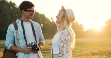 Portre alanında günbatımı üzerinde duran, birbirine bakarak ve kameraya gülümseyen beyaz genç erkek ve kadın turistlerin.