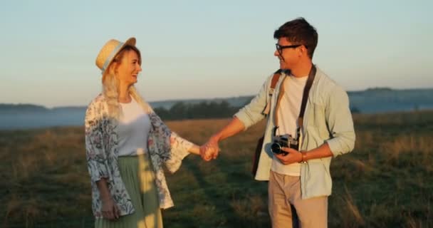 Portraitaufnahme des romantischen jungen verliebten Paares, das Hand in Hand auf dem Feld geht und sich küsst. Sommersonnenuntergang. — Stockvideo
