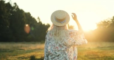 Arkadan alan sunset Bulvarında yürürken sonra dönüm ve kameraya gülümseyen şapkalı sarışın genç kadın görünüşü.