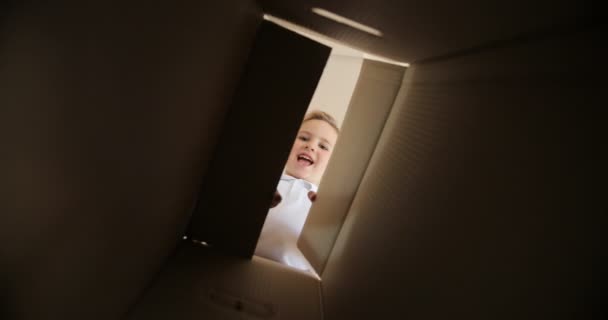 Flyttar till en ny lägenhet. lyckligt barn tittar in i en kartong. Pojke öppnar en skifte låda med olika versioner av känslor och att vara förvånad. — Stockvideo