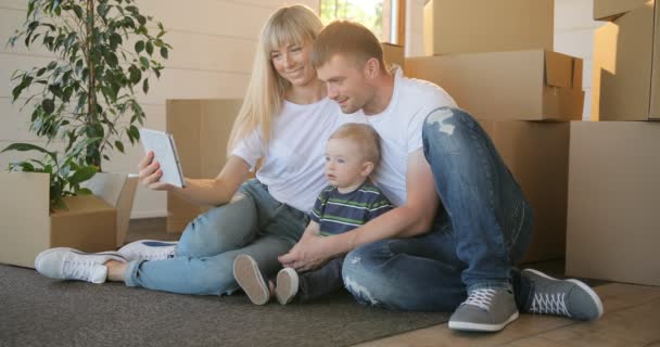 Mann und Frau und ihr Sohn ziehen in ein neues Zuhause. Hypothek, Menschen, Wohnungs- und Immobilienkonzept - glückliches Familienporträt mit Tablet-PC beim Umzug ins neue Haus — Stockvideo