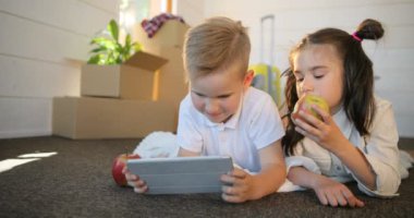 PC tablet ile birlikte oynayan mutlu kardeşler çocuk. Kız ve erkek kardeşim yeni evde tablet birlikte oyun oynamak. Kutuları backgroud