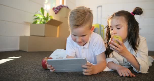 Glada syskon barn leker med pc tablet tillsammans. Bror och syster spela tillsammans i spel på tabletten i nya hus. Rutorna backgroud — Stockvideo