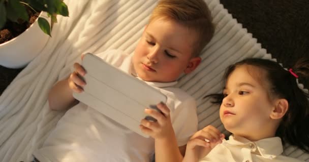 Ovanifrån av bror och syster med surfplatta liggandes i golvet. Små barn tittar på Touchpad hemma — Stockvideo