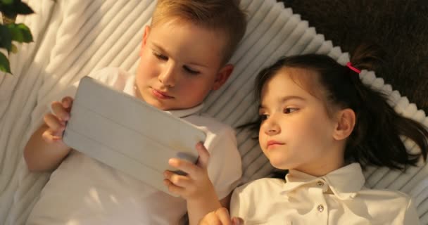 Bovenaanzicht van broer en zus met behulp van Tablet PC liggend in de vloer. Portret van kleine kinderen kijken thuis touchpad — Stockvideo