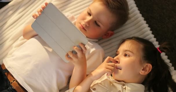 Pohled shora na bratra a sestru pomocí tabletu vleže v podlaze. Malé děti při pohledu na touch pad doma — Stock video
