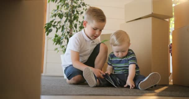 Retrato de dos niños divirtiéndose jugando o leyendo desde una tableta en su nueva casa. Los hermanos están interesados en usar y jugar tableta digital. Educación, hipoteca, vivienda y concepto de bienes raíces . — Vídeo de stock