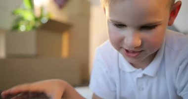 Oğlan yerde, yeni ev, karton kutuları arka plan yatarken sırasında dijital tablet kullanma.