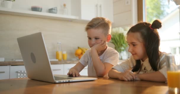 Porträtt av två leende skolbarnen använder bärbar dator i köket. Hem, skola, utbildning koncept. Pojke och flicka löpande laptop — Stockvideo