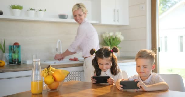 Счастливый семейный дом, младшие сестра и брат вместе пользуются мобильным телефоном. Мама с детьми смеются смотреть смешное видео . — стоковое видео
